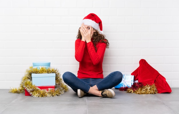 Dziewczyna w święta Bożego Narodzenia, siedząc na podłodze obejmujących oczy i patrząc przez palce