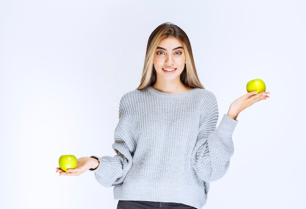 Dziewczyna w szarej bluzie, trzymając w ręku zielone jabłko.