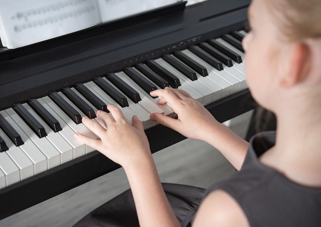 Dziewczyna w szarej sukience gra na pianinie elektronicznym na księdze muzycznej. Strona główna Szkoła Obraz z bliska