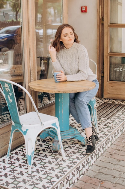 Zdjęcie dziewczyna w szarym swetrze siedzi przy stoliku w kawiarni i pije kakao i rozkoszuje się aromatem