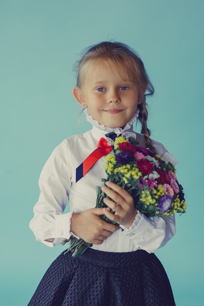 Dziewczyna w szkolnej spódnicy i bluzce z bukietem kwiatów. Powrót do szkoły