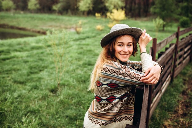 Dziewczyna w ubraniach z etnicznymi wzorami pozuje w natury ścianie. Portret uśmiechnięta młoda kobieta w boho kapeluszu. bliska portret dziewczynki w kapeluszu na ścianie lasu w deszczowy dzień.