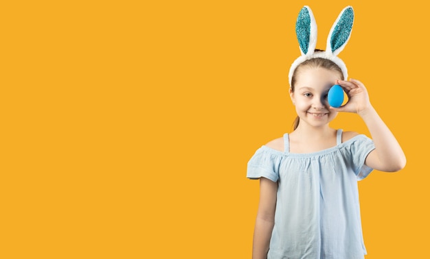 Dziewczyna w uszach królika na głowie trzyma w rękach niebieskie jajko i zamyka nim jedno oko