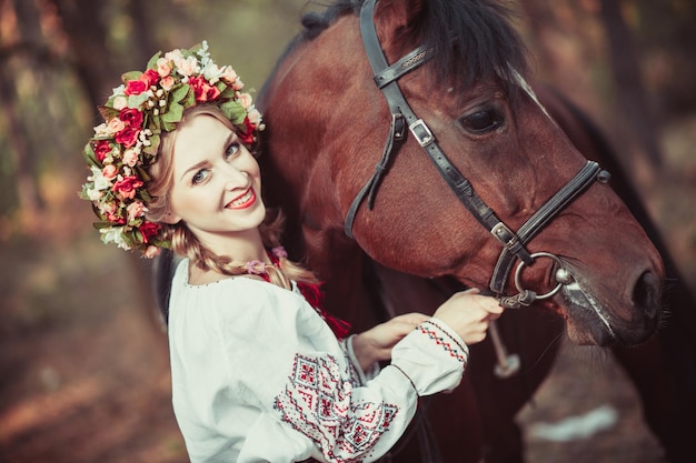 Dziewczyna w wianku i haftowanej koszuli z koniem w lesie