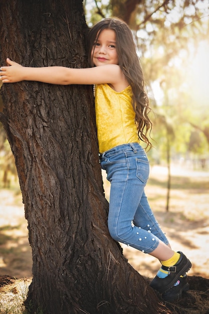 Dziewczyna w wieku przedszkolnym przytula drzewo w lesie motyw dnia dziecka międzynarodowy dzień drzewa