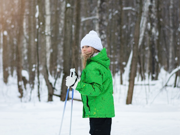 Dziewczyna w zielonej kurtce w słońcu w zimowym lesie na nartach