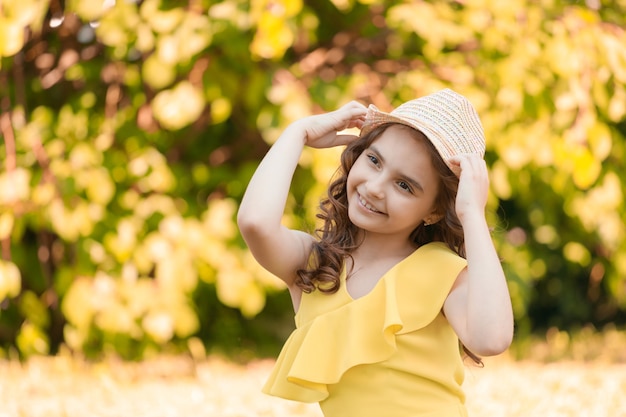 Dziewczyna w żółtych ubraniach i kapeluszu siedzi na trawie w parku latem. Zdjęcie wysokiej jakości