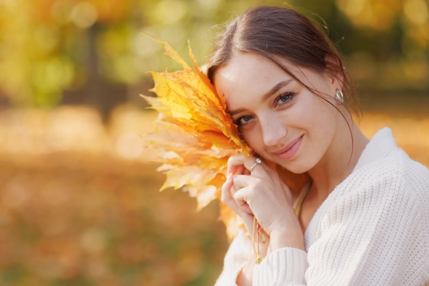 Dziewczyna w żółtych ubraniach w jesiennym parku raduje się jesienią, trzymając w dłoniach ciepłe żółte liście