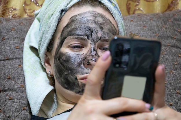 Zdjęcie dziewczyna wieczorem założyła sobie na twarz maseczkę oczyszczającą i leżała oglądając telefon