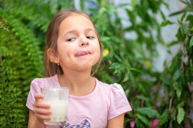 Dziewczyna wypiła ze szklanki kefir lub mleko i oblizała wargi językiem. Wąsy Kefir