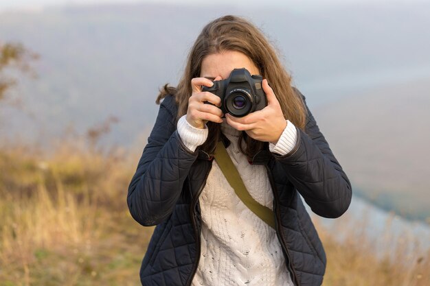 Zdjęcie dziewczyna z aparatem w dłoniach w zabawnej pozie robi ramkę paparazi z aparatem w dłoniach na ognisku w górach