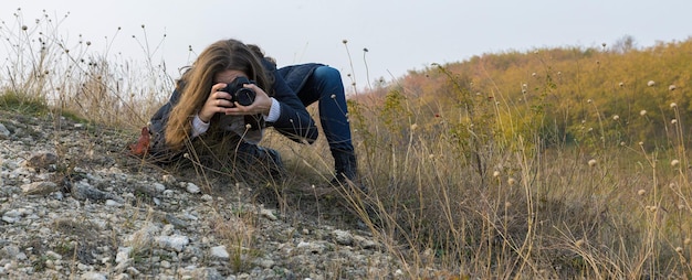 Dziewczyna z aparatem w dłoniach w zabawnej pozie robi ramkę Paparazi z aparatem w dłoniach na ognisku w górach