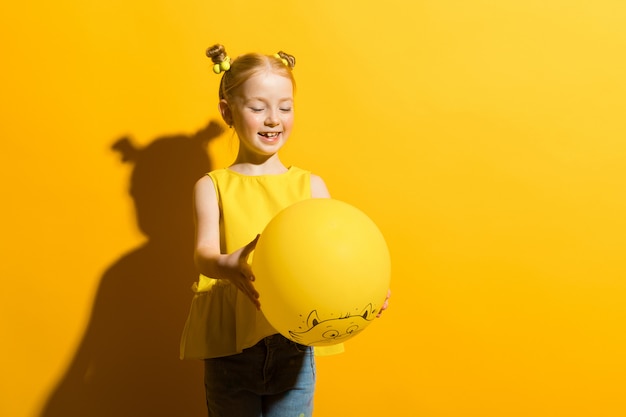 Dziewczyna z czerwonym włosy na żółtym tle. Dziewczyna trzyma w dłoniach i patrzy na żółty balon.