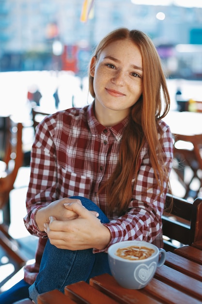 Dziewczyna z dużą filiżanką kawy przy drewnianym stołem outdoors