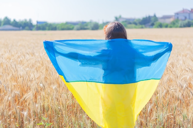 Zdjęcie dziewczyna z flagą ukrainy w widoku z tyłu pola pszenicy. pojęcie ukraińskich świąt narodowych. dzień niepodległości ukrainy.