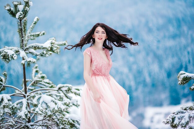 Dziewczyna z kasztanowymi włosami, niebieskimi oczami i różową sukienką na tle zimowych gór