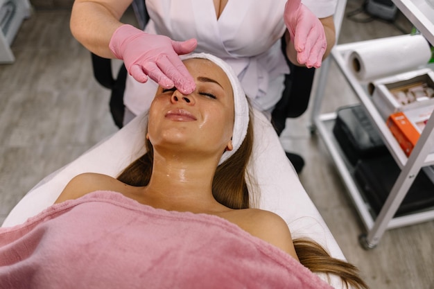 Dziewczyna z kosmetyczką w salonie spa Kosmetyczka wykonuje zabiegi kosmetycznestosowanie kremu kosmetycznego Kosmetologia piękno twarzy Pojęcie pielęgnacji skóry twarzy Artykuł o kosmetologii