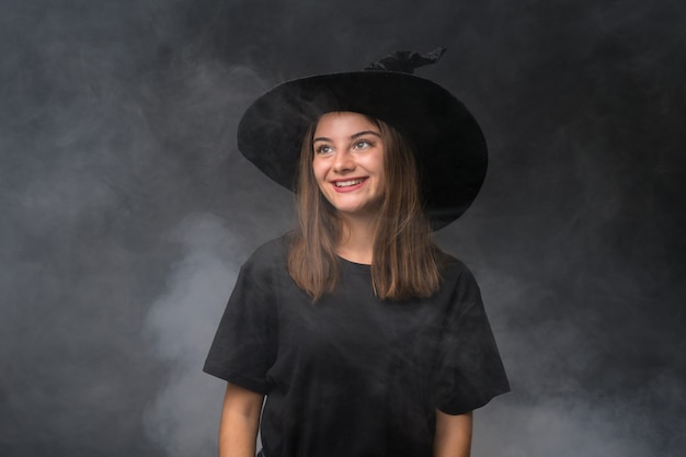Dziewczyna z kostiumem czarownicy na imprezy halloween na pojedyncze ciemne ściany, śmiejąc się i patrząc w górę