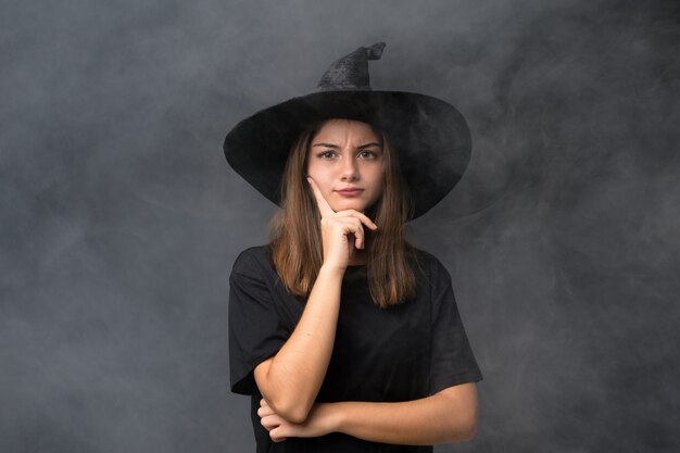 Dziewczyna z kostiumem wiedźmy na imprezy Halloween na pojedyncze ciemne ściany myśląc pomysł