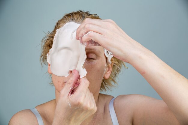 Dziewczyna z maską na twarz patrząc na kamery na białym tle. Procedura kosmetyczna. Spa i kosmetologia.