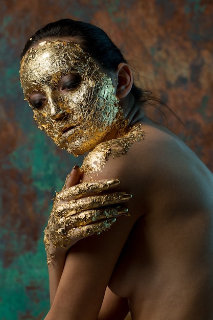 Dziewczyna z maską na twarzy wykonaną ze złotego liścia Ponury portret studyjny brunetki na abstrakcie