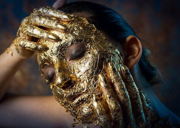 Dziewczyna z maską na twarzy wykonaną ze złotego liścia Ponury portret studyjny brunetki