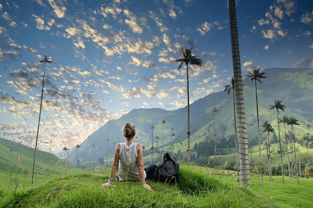 Dziewczyna z plecakiem siedząca na zielonej trawie oglądając dolinę palmową