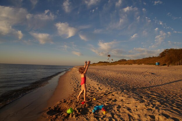 Zdjęcie dziewczyna z podniesionymi ramionami stojąca na plaży na tle nieba podczas zachodu słońca