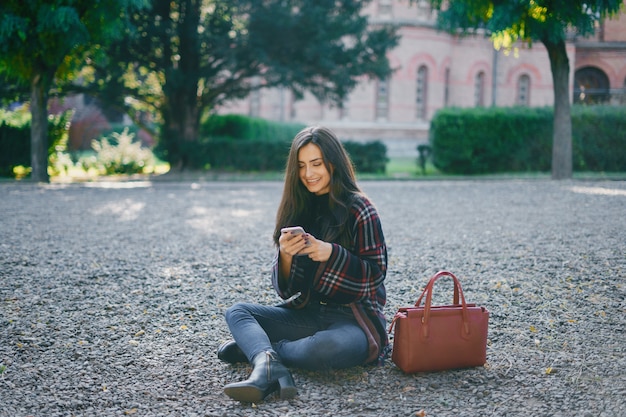 dziewczyna za pomocą swojego telefonu komórkowego podczas spaceru przez park podczas jesieni