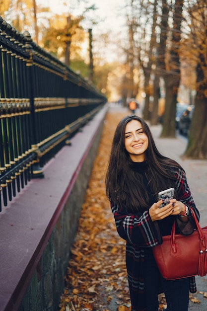 dziewczyna za pomocą swojego telefonu komórkowego podczas spaceru przez park podczas jesieni