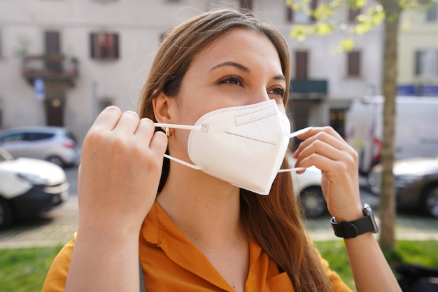 Dziewczyna zakłada maskę ochronną na zewnątrz. Zamknij się młoda kobieta ubrana w maskę medyczną KN95 FFP2 na ulicy miasta.