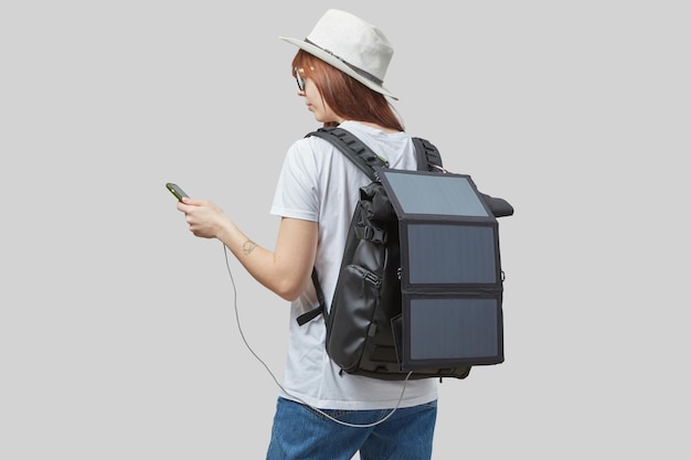 Zdjęcie dziewczyna ze smartfonem w rękach niosąca plecak z ładującym panelem słonecznym