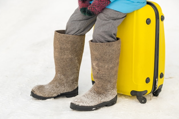 Dziewczyna zimą w filcowych butach siedzi na walizce w mroźny, śnieżny dzień