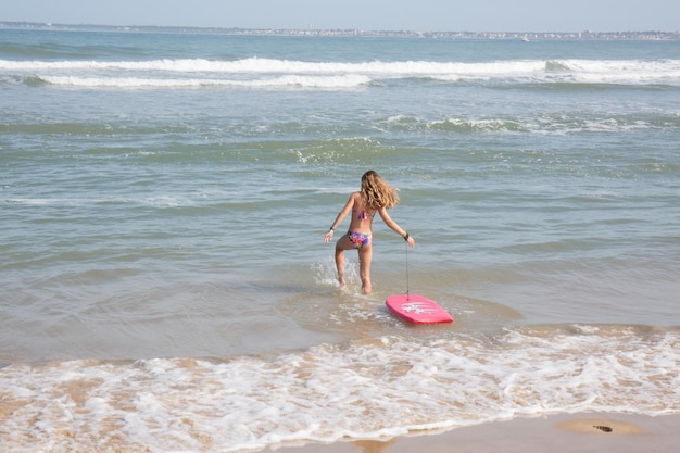 dziewczynka bawi się w wodzie morskiej z deską surfingową