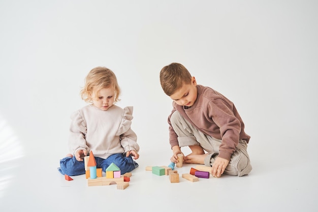 Dziewczynka bawi się wesołym dzieckiem z zabawkami drewnianymi kostkami na białym tle Dzieci uśmiechają się i bawią razem