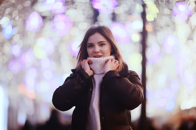 dziewczynka lampki choinkowe wieczorne udekorowane miasto, młoda modelka na tle miejskich dekoracji i girland, nocne lampki miejskie