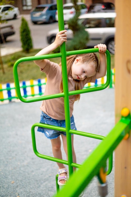 Dziewczynka na wielokolorowym placu zabaw dla dzieci na dziedzińcu wielopiętrowego domu latem bawi się bawiąc się i wspinając po schodach letnie wakacje