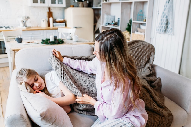 Dziewczynka śpi na sofie, jej mama kradnie koc córce, opiekę i uwagę