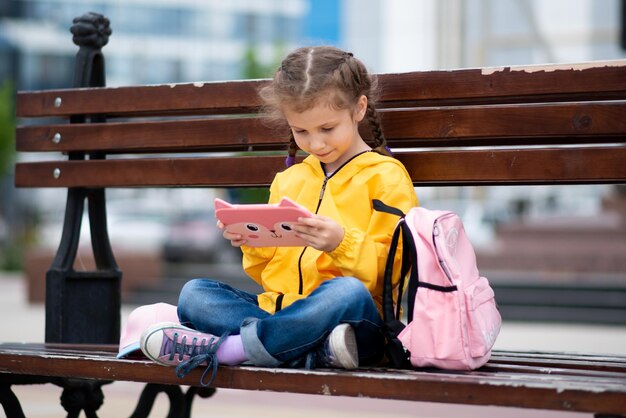 Dziewczynka trzymająca w dłoniach tablet Siedzi na zewnątrz na ławce Dzieci korzystają z technologii