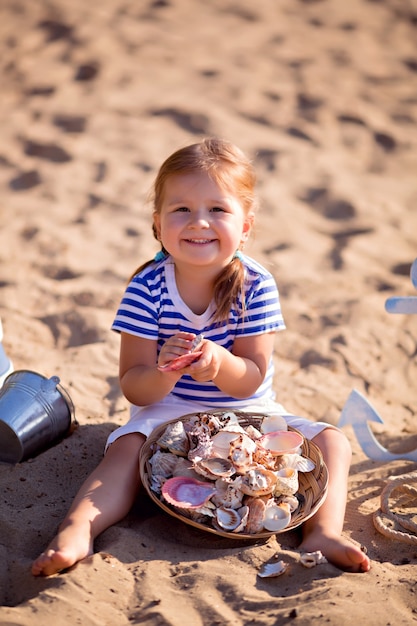 Dziewczynka ubrana jak żeglarz na piaszczystej plaży z muszelkami nad morzem