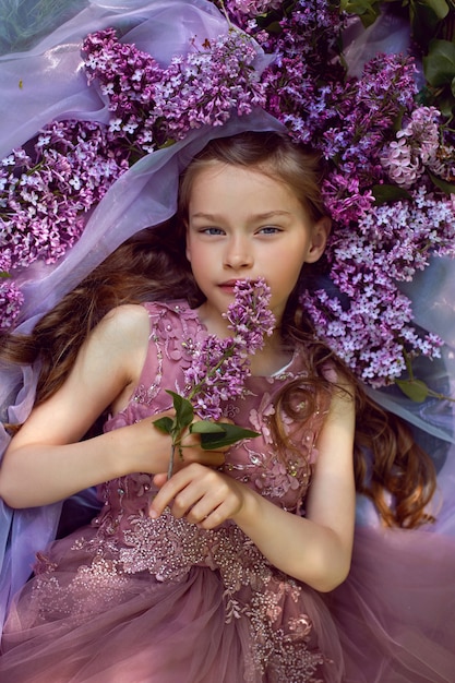 Dziewczynka W Fioletowej Kwiecistej Sukience Leży Na Ziemi Wśród Bzów Na Welonie Wiosną