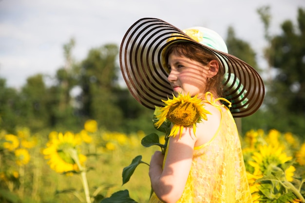 Dziewczynka w kapeluszu i żółtych ubraniach na polu ze słonecznikami