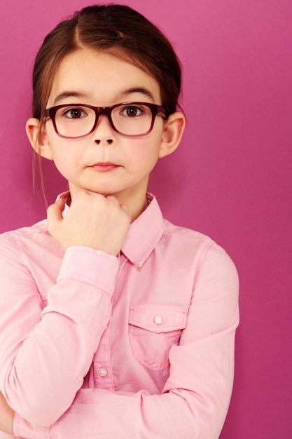 Dziewczynka w okularach portretowych i myśląca z pytającym wyrazem inteligencji i wizją odizolowana na różowym tle Inteligentny maniakiem lub frajerem z dziewczyną w studio zamyślony w okularach