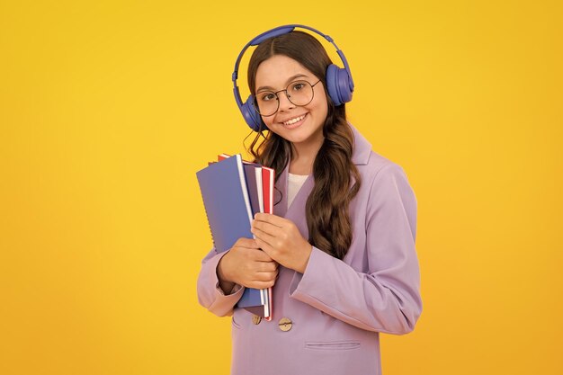 Dziewczynka w wieku szkolnym ze słuchawkami i książką isoalted na żółtym tle