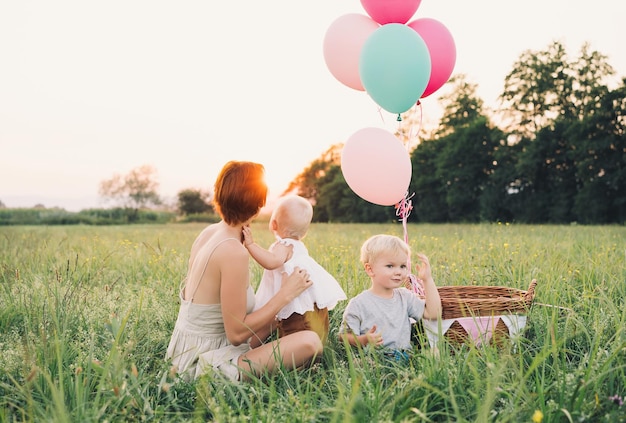 Dziewczynka w wiklinowym koszu z balonami w słońcu o zachodzie słońca Matka i dziecko na zewnątrz Pierwsze urodziny Rodzina świętuje jednoroczne dziecko na naturze Zdjęcie zdrowych snów wakacje wakacje