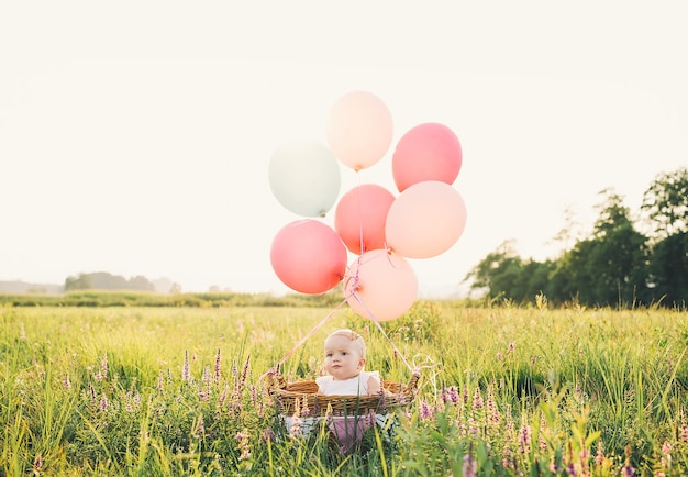 Dziewczynka w wiklinowym koszu z różowymi balonami w słońcu latem Szczęśliwe dziecko na naturze Pierwsze urodziny Rodzina świętuje jednoroczne dziecko na świeżym powietrzu Zdjęcie z dziecięcych marzeń wakacje