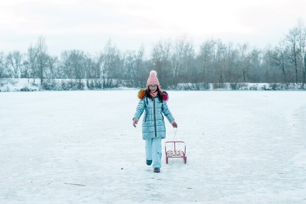 Dziewczynka z saniami spodek na zewnątrz w zimowy dzień, gry zimowe. Dziewczyna z saniami. Zimowy spacer.