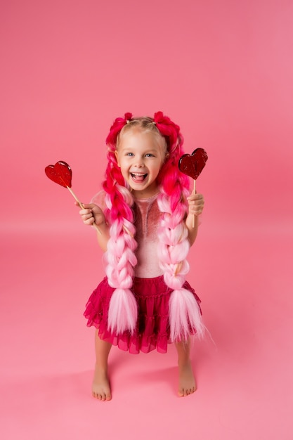 Dziewczynka Z Warkoczami Różowego Kanekalonu Trzyma Lollipopa W Kształcie Serca Na Różowym Tle