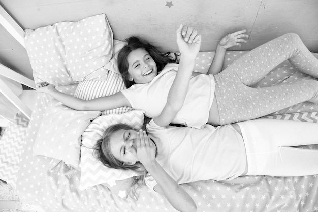 Dziewczynki dzieci leżą na łóżku z uroczymi poduszkami widok z góry Koncepcja imprezy w piżamie Dziewczęce się bawią Dziewczęce sekrety uczciwi i szczerzy Przyjaciele wesoły zabawny nastrój zabawne grymasy Najlepsi przyjaciele na zawsze