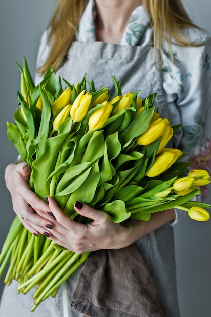 Dziewczyny kwiaciarnia trzyma wiązkę żółci tulipany. Florystyczny. Szare tło